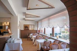 A restaurant with tables set for dining, a counter with a display, and a view through the window.