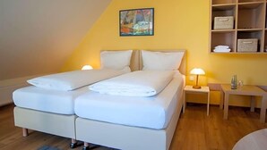 A double bed with white bedding, a bedside table with a lamp, a small shelf with folded towels, and a painting on the wall. - Hotel Elbblick (Geesthacht)