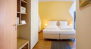 A hotel room with a curved bed, bedside lamps, a wooden floor, and a shelf with folded towels.