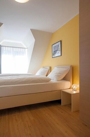 A bedroom with a bed, a bedside table, a wall-mounted picture, and a window with curtains.