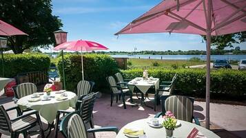 An outdoor patio with round tables and chairs, umbrellas, and a view of a lake.