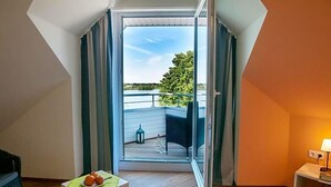 A room with a sliding glass door leading to an outdoor balcony with a view of a tree and a body of water. - Hotel Elbblick (Geesthacht)