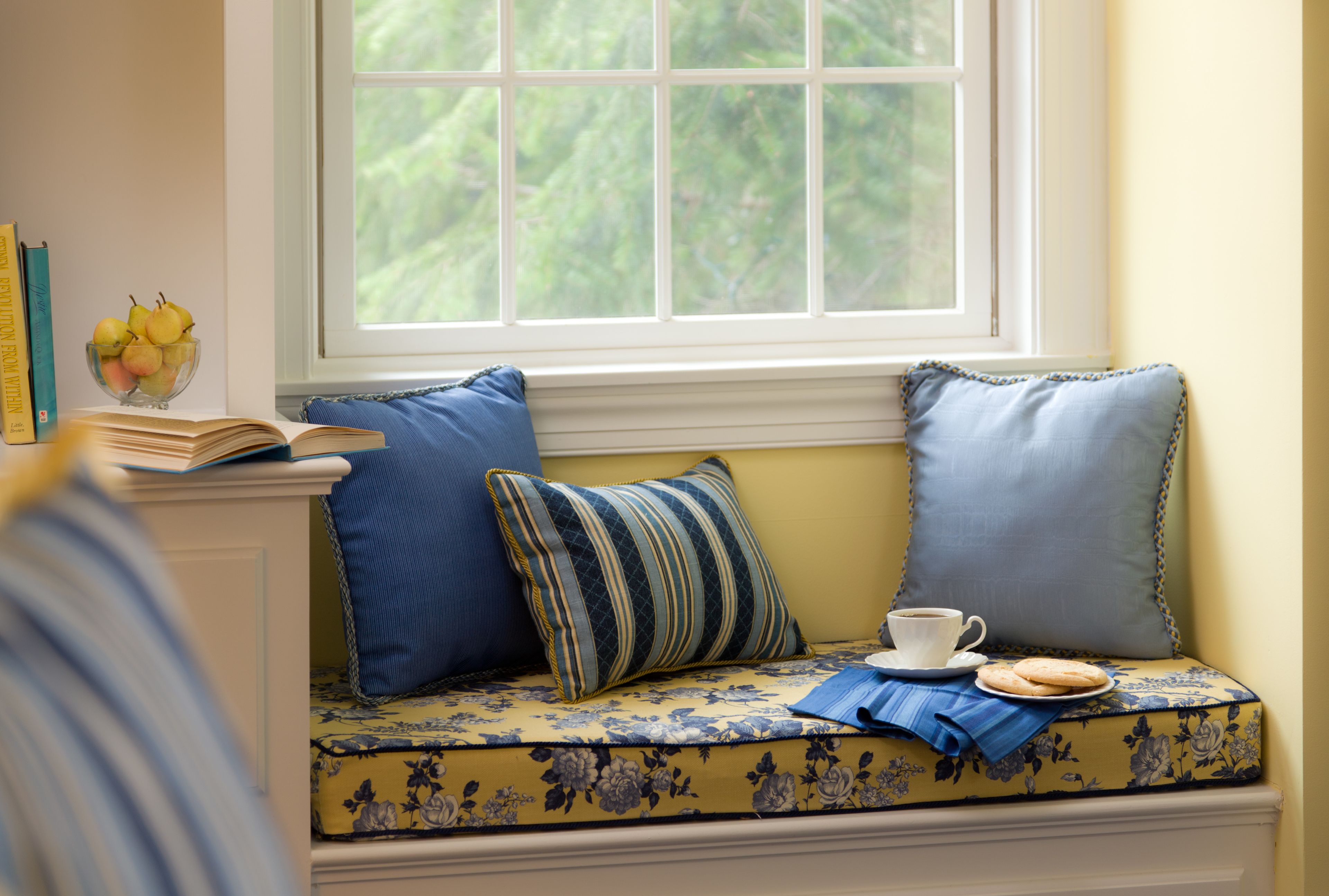 A cozy seating area with a window, a bowl of fruit, and a cup of tea.