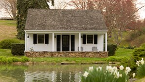 A white house with a stone foundation, a pond in front, and daffodils in the foreground. - The Inn at Whitewing Farm (West Chester)