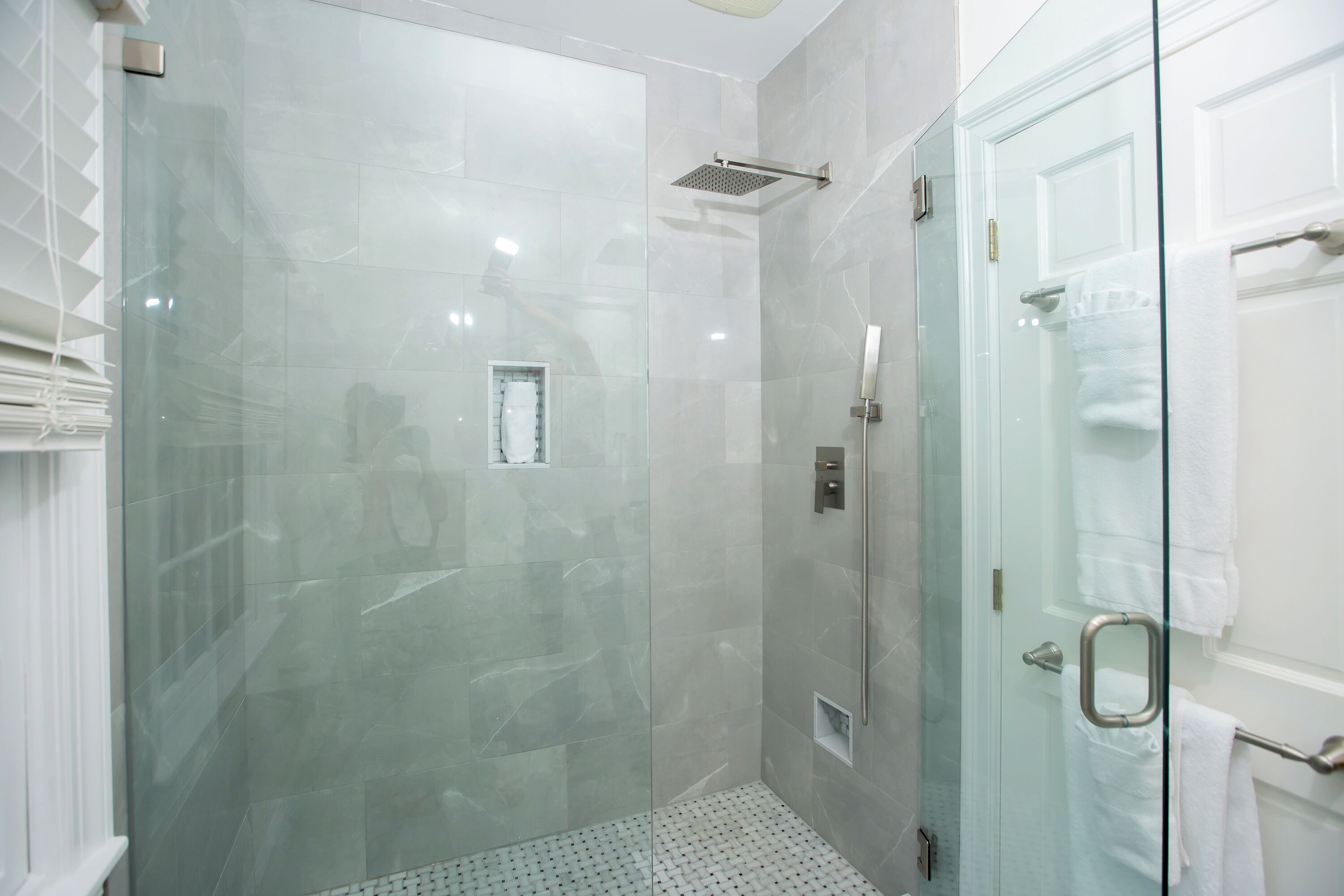 A modern bathroom with a glass-enclosed shower, a white tiled floor, and a glass door with a towel rack.