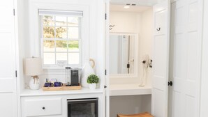A white bathroom with a window, a mirror, a sink, a towel rack, and a wooden stool. - The Inn at Whitewing Farm (West Chester)