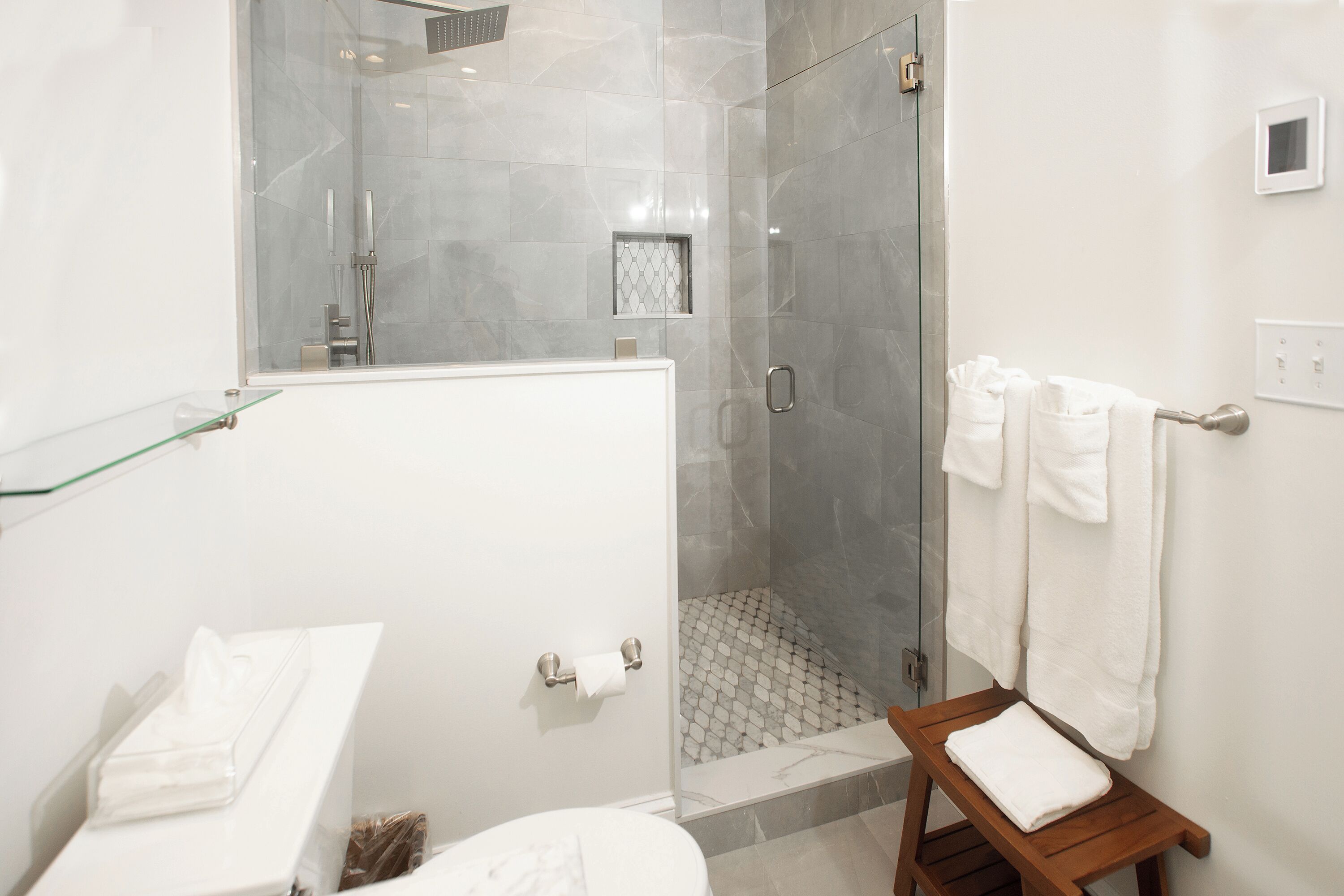 Un baño moderno con ducha acristalada, un lavabo blanco y un banco de madera con una toalla.