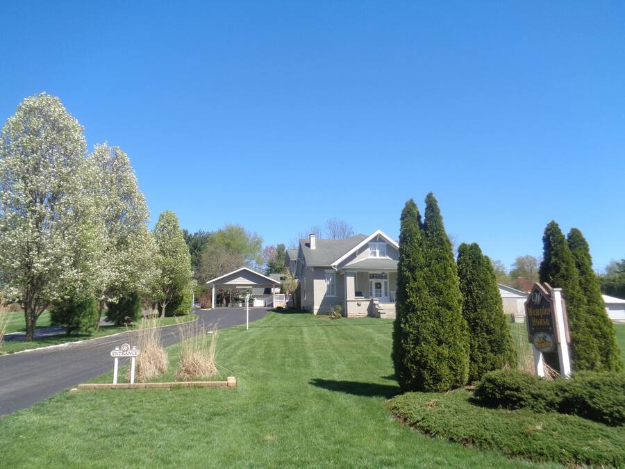 A residential house with a covered porch, a well-maintained lawn, and a sign indicating the entrance.