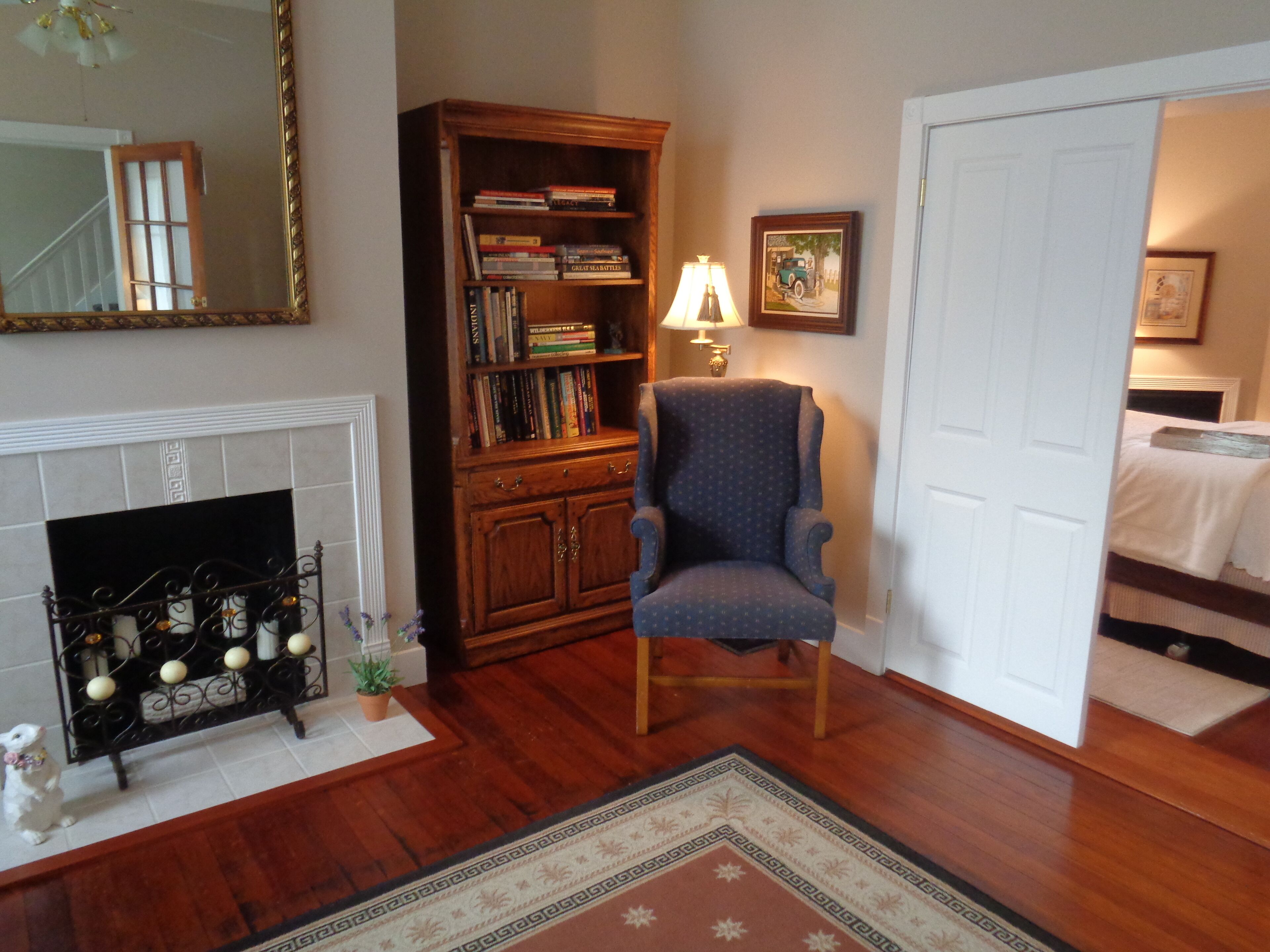 A room with a fireplace, a bookshelf, a chair, and a door leading to another room.
