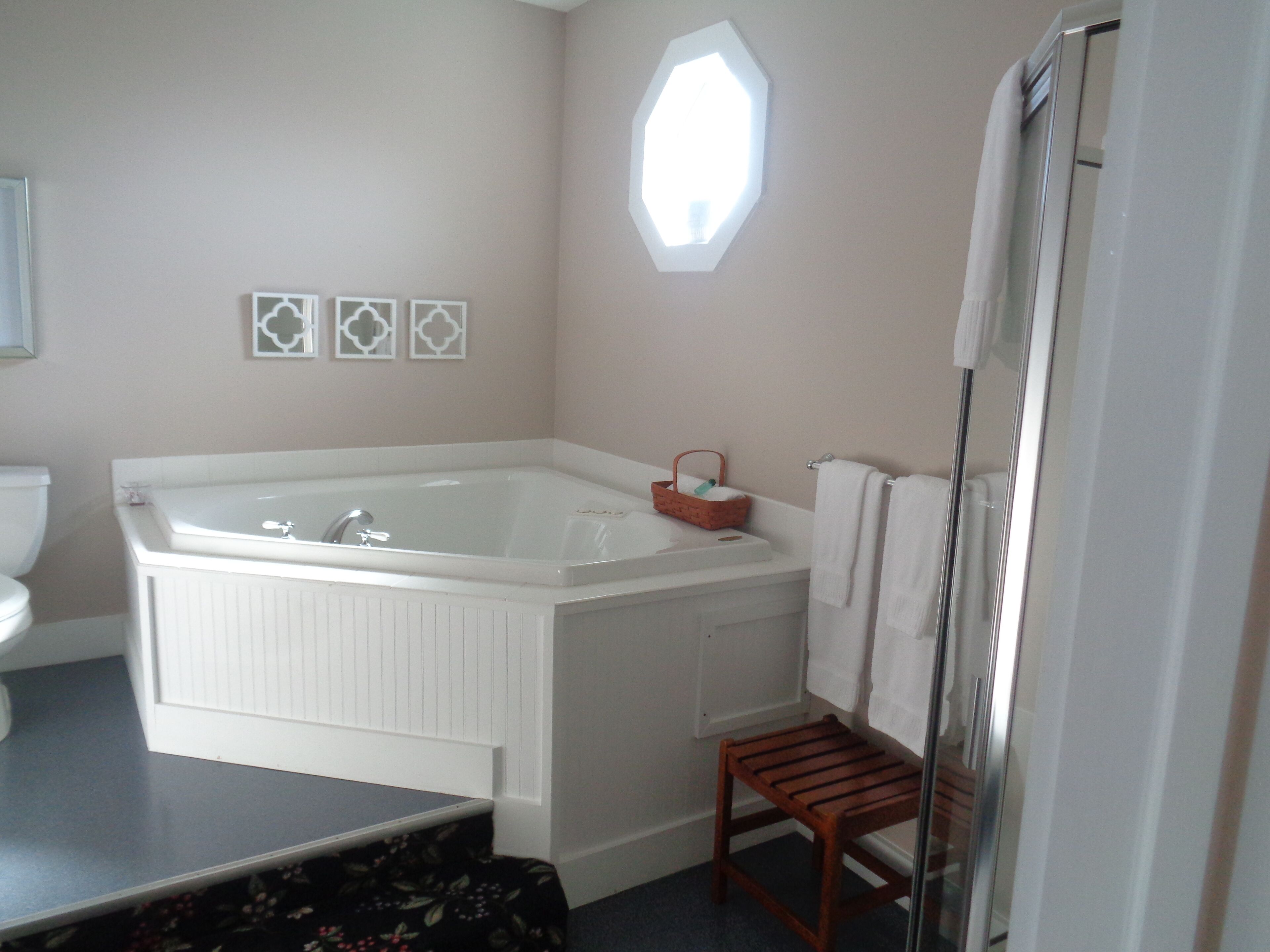 A bathroom with a large bathtub, a small wooden stool, a white sink, and a toilet.