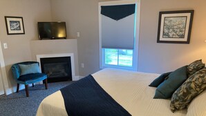 Een slaapkamer met een groot bed, een televisie, een open haard en twee ingekaderde foto’s aan de muur.