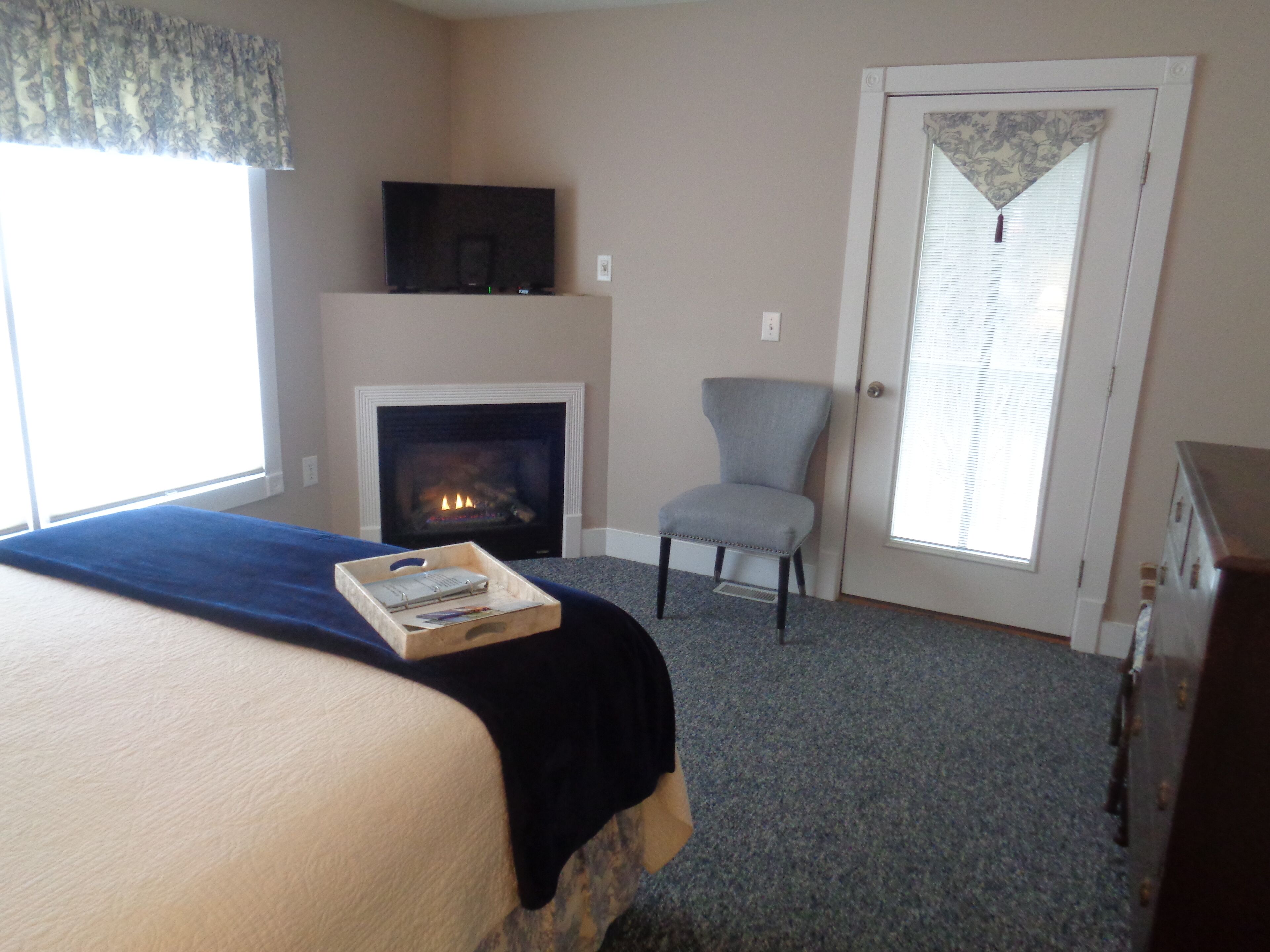 A bedroom with a bed, a fireplace, a chair, and a door with blinds.