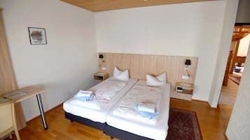 A double bed with white bedding and two pillows, a bedside table with a lamp, and a wooden headboard.