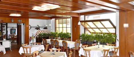 A restaurant with wooden ceiling beams, white tablecloths, and wooden chairs.