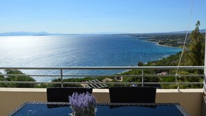 Un balcon avec une table et des chaises en verre, offrant une vue sur la côte et un ciel dégagé.
