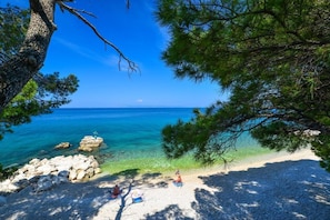 A beach with clear turquoise water, rocky outcrops, and a few people relaxing on the sand. - Apartments Denise Podgora (Podgora)