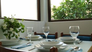 Mesa de jantar posta com pratos, tigelas e copos de vinho brancos, com um vaso de flores brancas à esquerda.