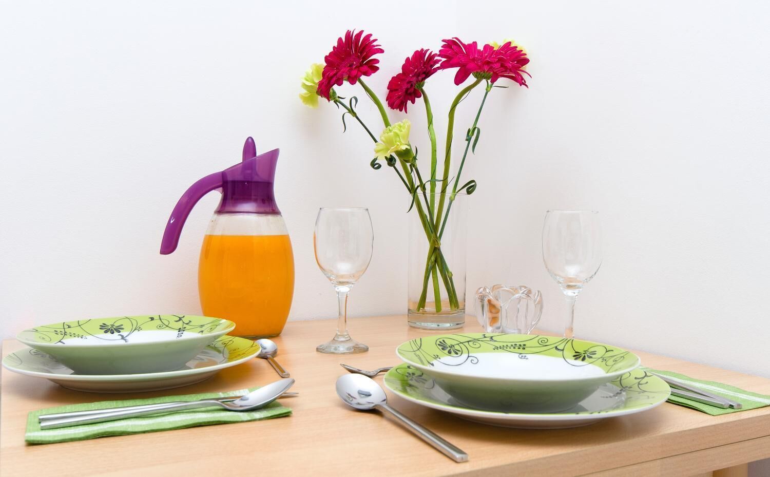 Une table dressée avec des assiettes, une carafe de jus d’orange et un vase rempli de fleurs.