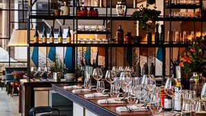 Una zona de bar con varios taburetes, una barra larga y estantes llenos de botellas y vasos.