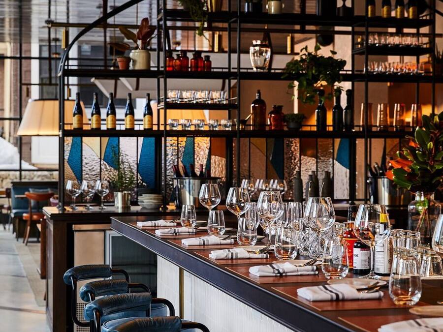 A bar area with multiple stools, a long counter, and shelves stocked with bottles and glasses.