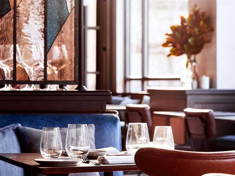 A restaurant interior with a blue sofa, dining tables with wine glasses, and pendant lighting.