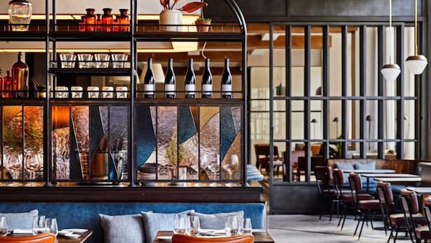 Un restaurante moderno con barra, distintos arreglos de asientos y una pared decorativa.