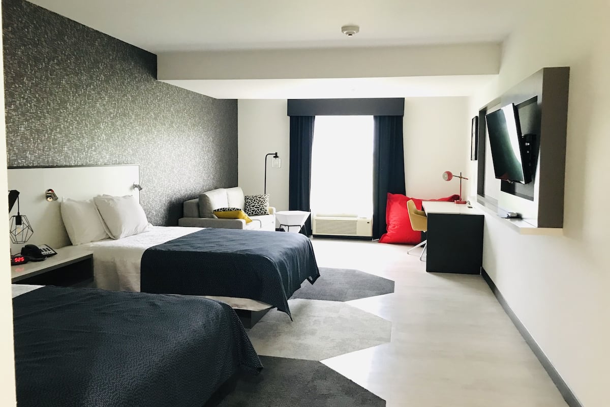 A modern hotel room with two beds, a desk, a TV, and a large window with curtains.