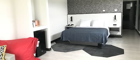 A modern hotel room with a bed, a red couch, a small table, and a black storage unit.