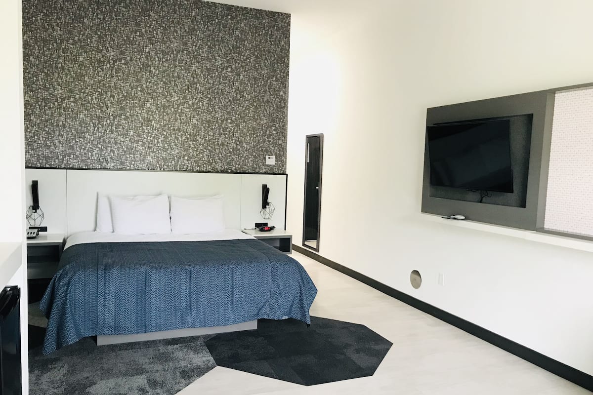 A modern hotel room with a large bed, a flat-screen TV mounted on the wall, and a patterned headboard.