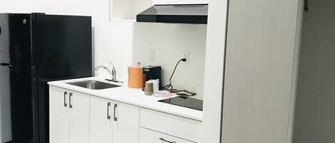 A compact kitchen with white cabinets, a black refrigerator, and a small countertop with a coffee maker.