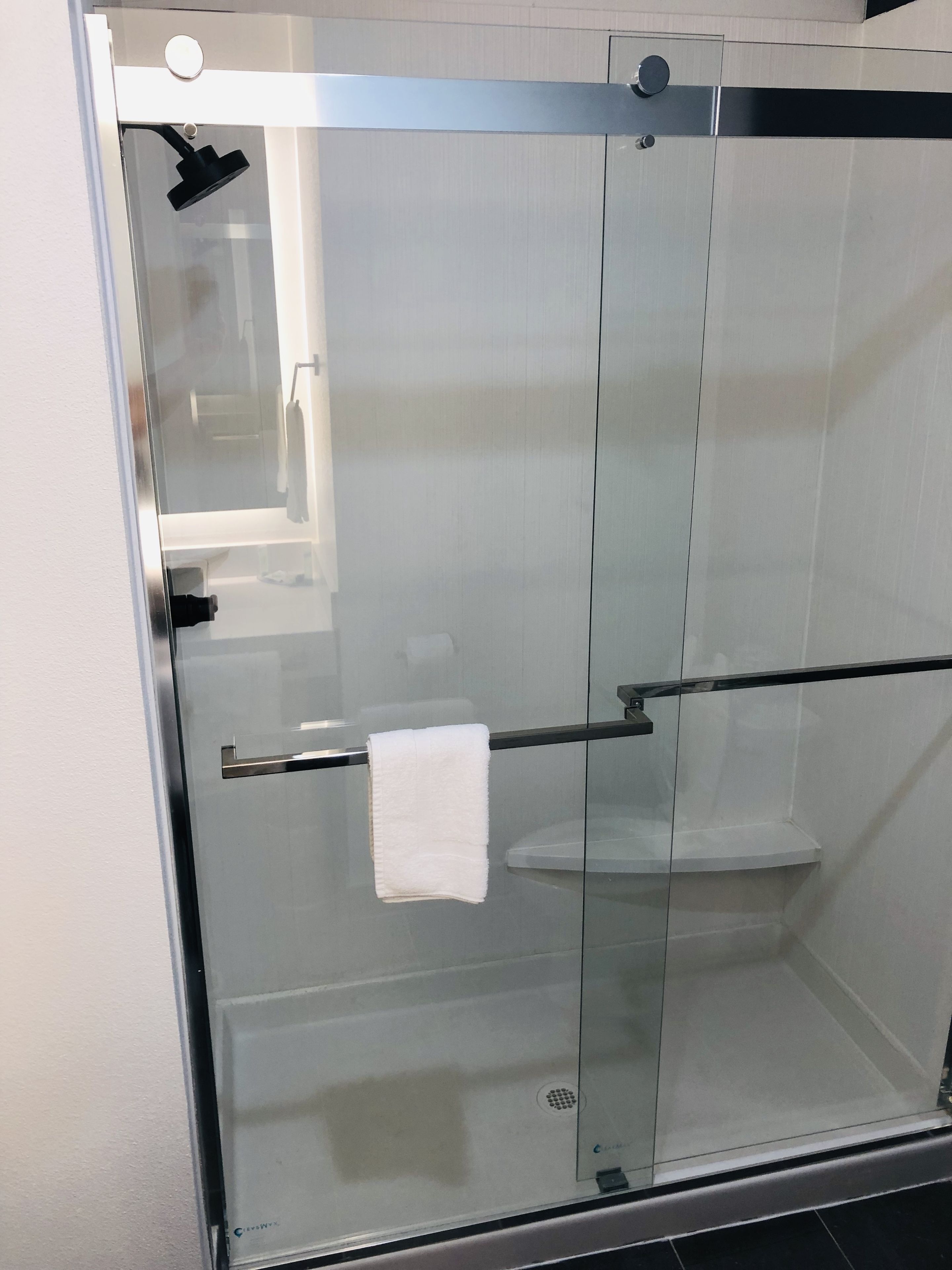 Un box de ducha con paredes de vidrio, un perchero y un inodoro a la vista a través del vidrio.