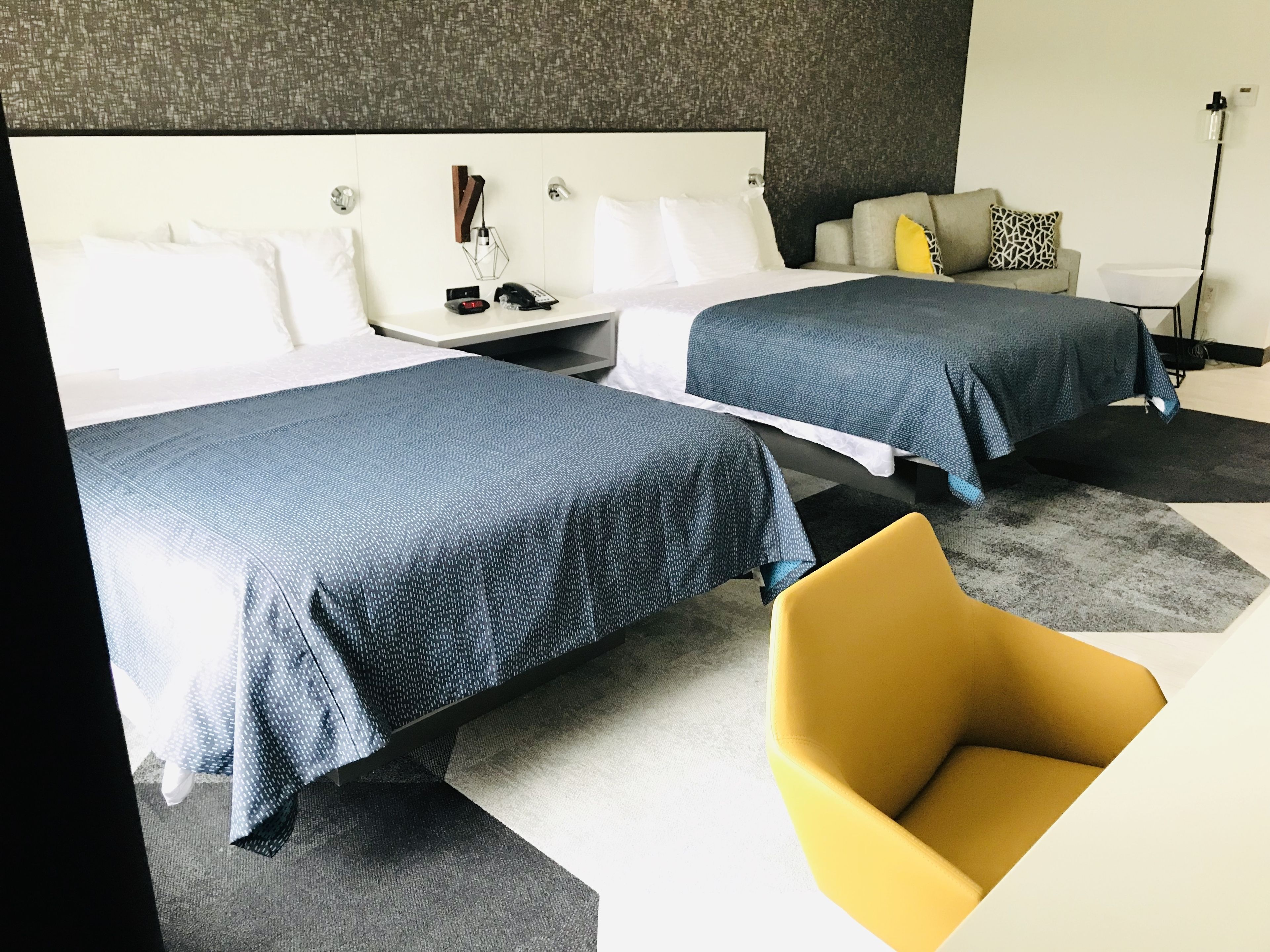 Ein Hotelzimmer mit zwei Betten, einem Nachttisch, einer Lampe und einem modernen Sessel.