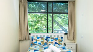 A neatly made bed with a geometric-patterned bedspread, a rolled white towel, and a window with curtains. - Hobson Lodge - Hostel (Auckland)
