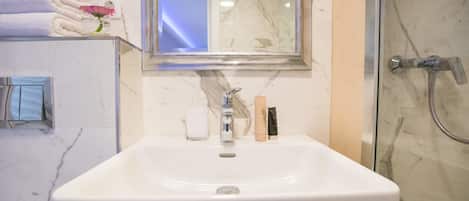 Un baño con un lavabo blanco, un espejo, un toallero con toallas dobladas y una zona de ducha.