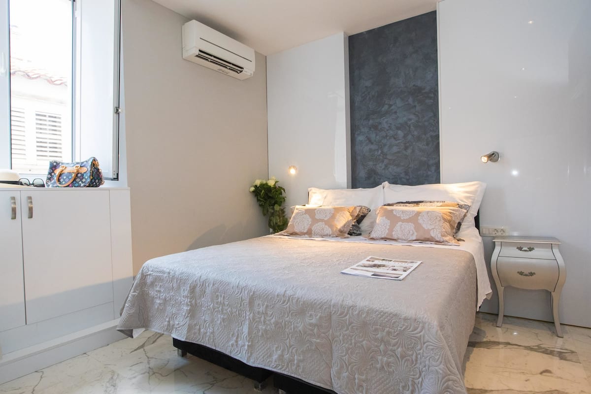 A neatly arranged bedroom with a bed, bedside table, and a window with a view.