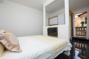 Quarto com cama, TV e vista para área externa com corrimão.