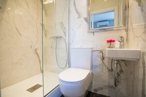 Un baño con ducha de vidrio, inodoro blanco y lavamanos con espejo.