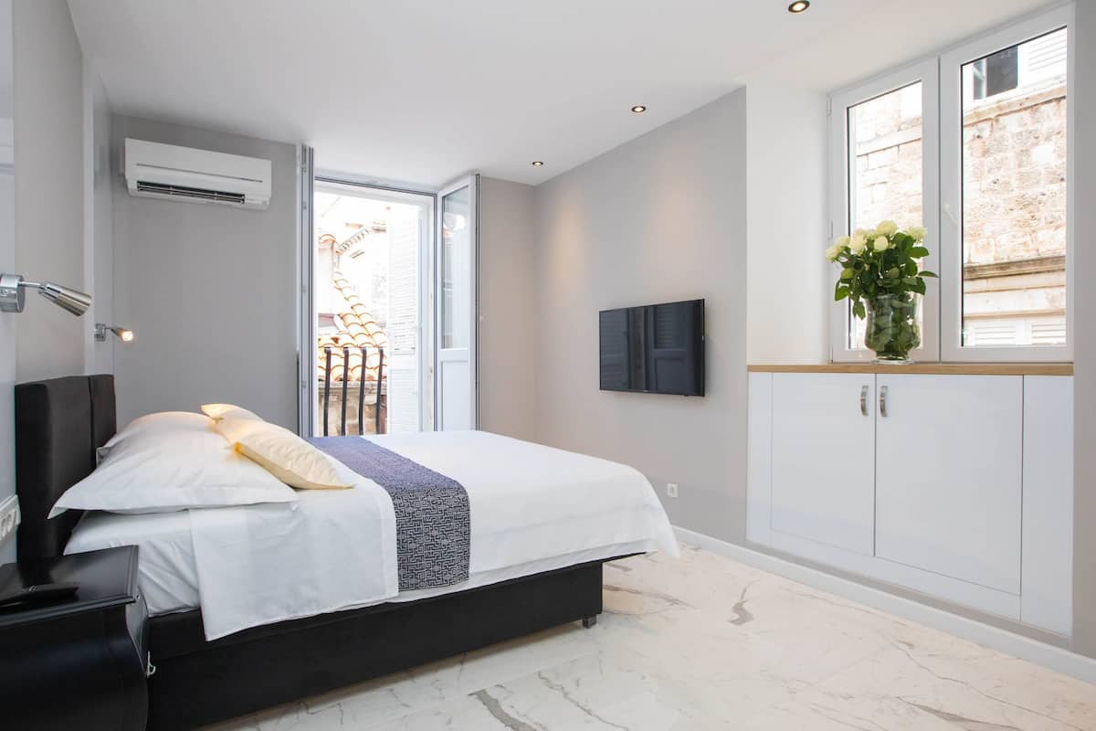 A bedroom with a bed, a TV, a wardrobe, and a window with a view.
