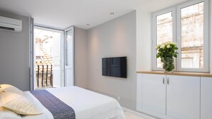 Un dormitorio con cama, televisor montado en la pared, ventana con planta y vistas al exterior.