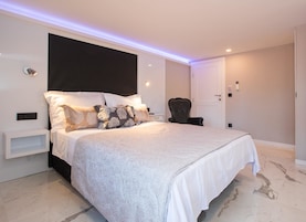 Um quarto moderno com uma cama grande, cabeceira escura e mesa de cabeceira branca.