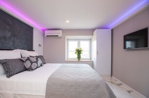 Quarto moderno com uma cama grande, uma janela com vista e uma TV na parede.