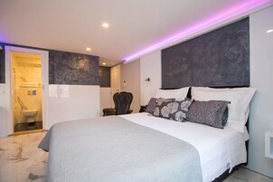 A modern bedroom with a large bed, a dark headboard, and a bathroom visible through an open door.