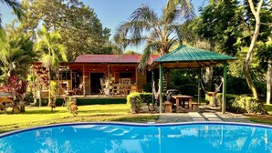 A pool surrounded by a patio area with a covered seating area and a building with a red roof.