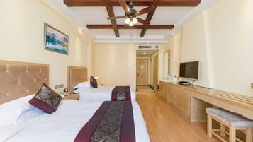 Quarto de hotel com duas camas, um ventilador de teto, uma TV e um banco de madeira.
