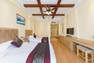 Habitación de hotel con dos camas, ventilador de techo, televisión y un banco de madera.