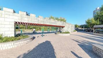 A paved walkway with a covered seating area, a stone wall, and a clear sky.