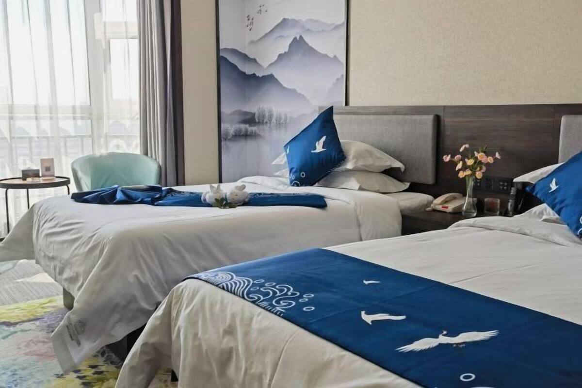 Habitación de hotel con dos camas, vistas a las montañas a través de la ventana, una mesita con un florero y una silla.