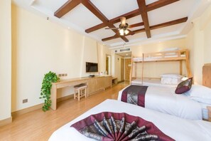 Ein Hotelzimmer mit Holzboden, einem Schreibtisch mit Stuhl, einem Fernseher, zwei Betten mit Kissen und einer Pflanze.