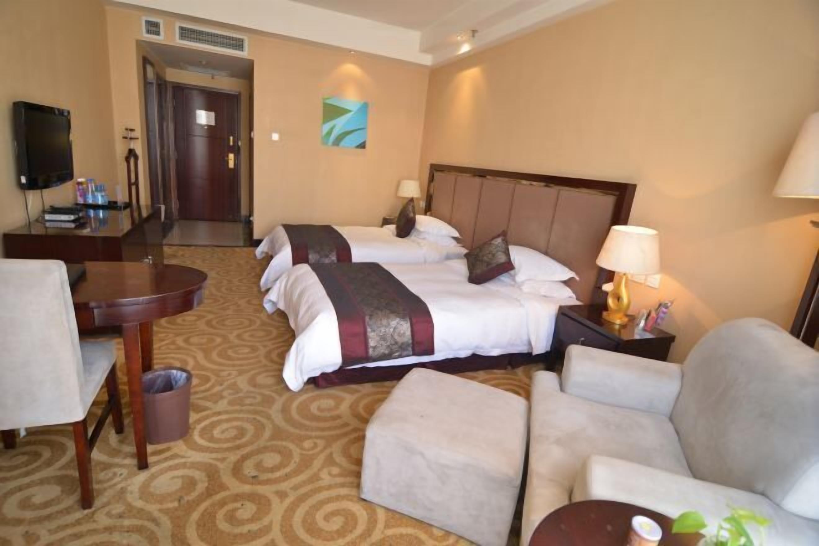 Ein Hotelzimmer mit zwei Betten, einem Fernseher, einem Schreibtisch und einem Stuhl.