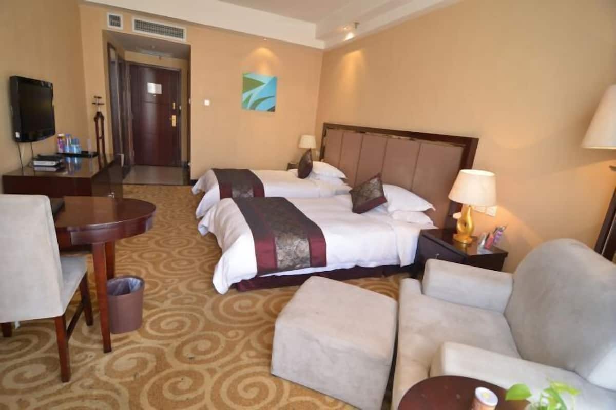 Quarto de hotel com duas camas, uma televisão, uma escrivaninha e uma cadeira.